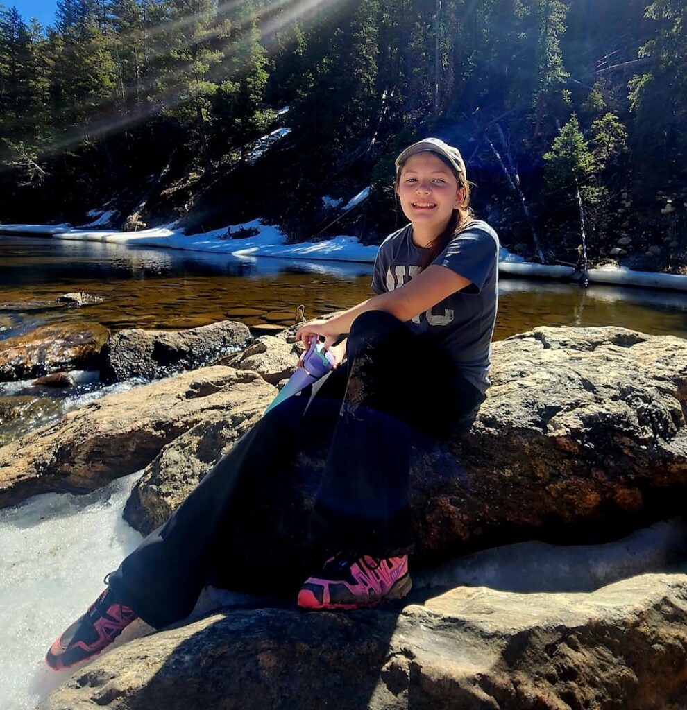 Elise Pellegrini on a hike, sitting on rocks near a river