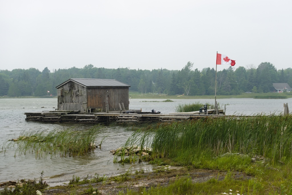 A dock with a tiny boat house and a Canadian flag on Lake Huron